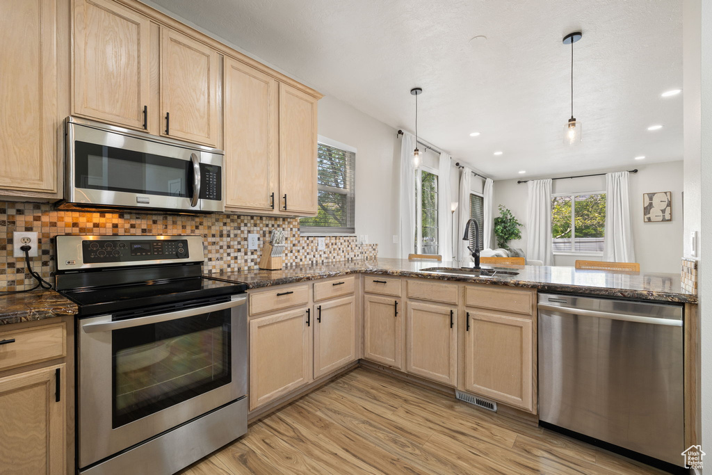 Kitchen with appliances with stainless steel finishes, light brown cabinets, a peninsula, decorative backsplash, and light wood finished floors