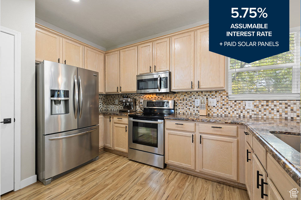 Kitchen featuring stainless steel appliances, light brown cabinetry, light wood finished floors, and dark stone counters