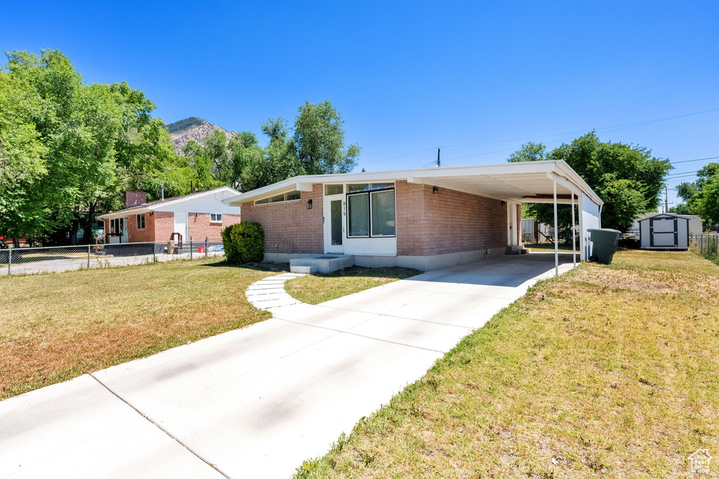 Mid-century inspired home featuring a storage shed, brick siding, driveway, and a carport