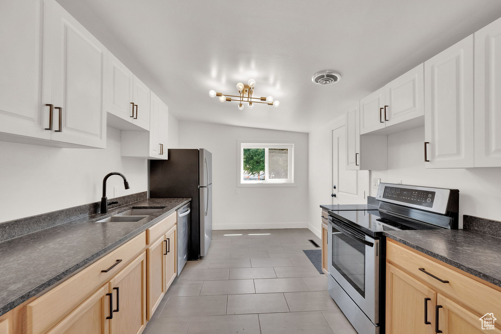 Kitchen with stainless steel appliances, light tile patterned floors, a chandelier, and light brown cabinetry