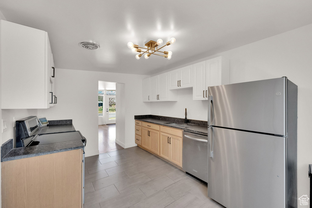 Kitchen with stainless steel appliances, a chandelier, dark countertops, and light tile patterned floors