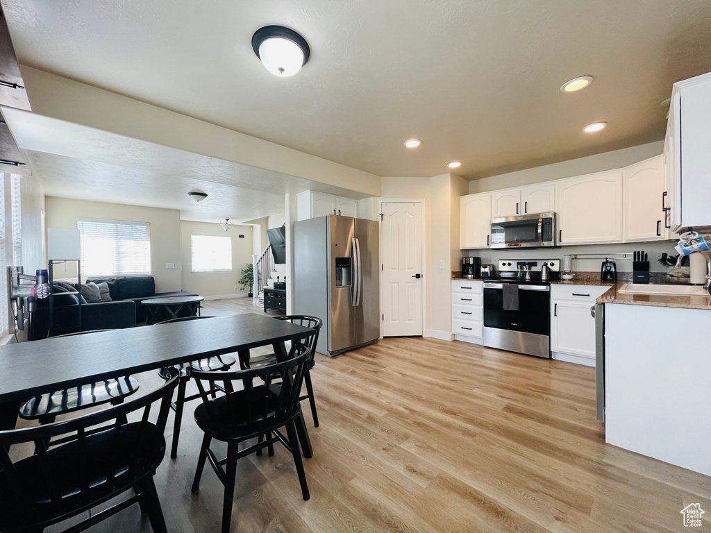 Kitchen featuring stainless steel appliances, light wood-type flooring, white cabinetry, open floor plan, and recessed lighting
