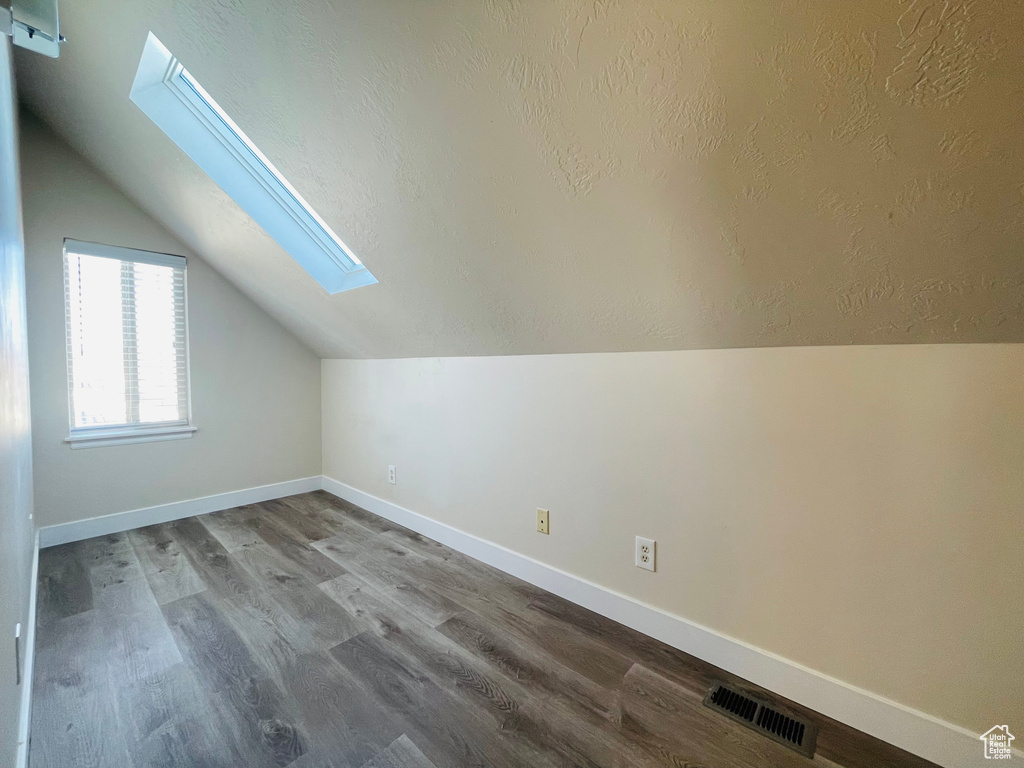Additional living space with a skylight, lofted ceiling, wood finished floors, and a textured ceiling