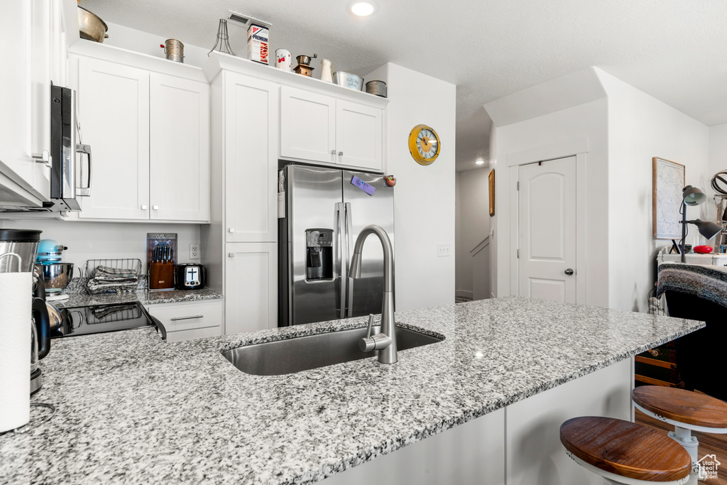 Kitchen featuring stainless steel appliances, a breakfast bar, white cabinets, light stone counters, and recessed lighting