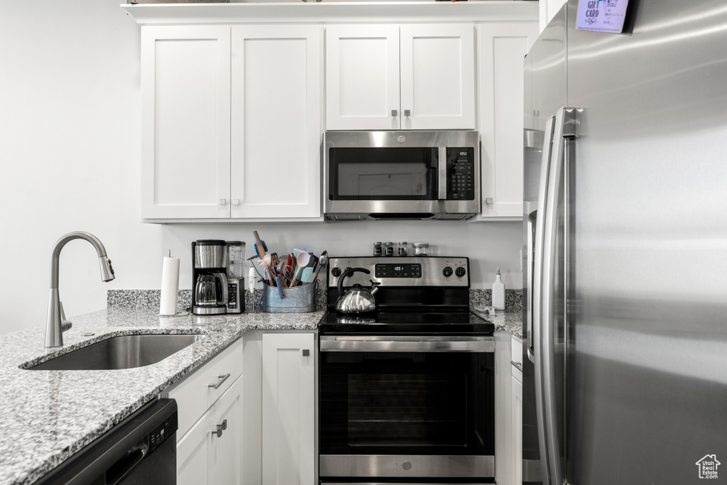 Kitchen with appliances with stainless steel finishes, white cabinetry, and light stone counters