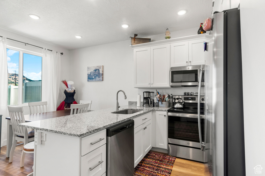 Kitchen with appliances with stainless steel finishes, a peninsula, white cabinets, light wood finished floors, and light stone countertops