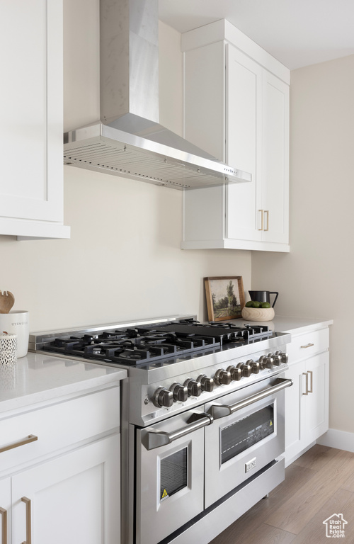 Kitchen with double oven range, wall chimney range hood, white cabinetry, light wood-style floors, and light countertops