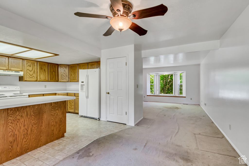 Kitchen featuring white appliances, under cabinet range hood, brown cabinetry, light countertops, and a ceiling fan
