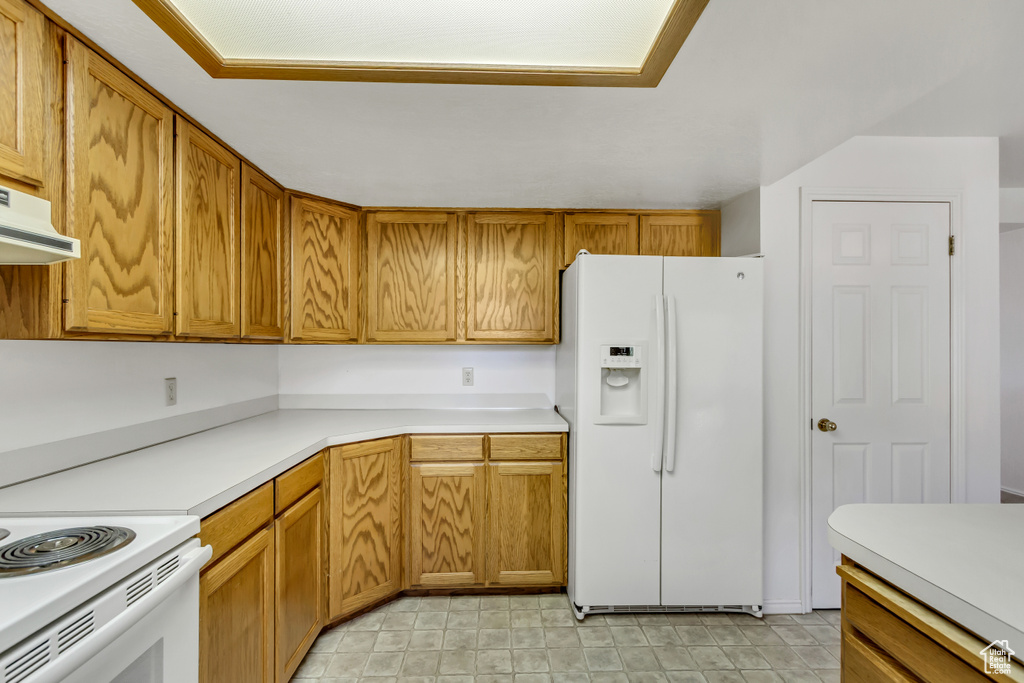 Kitchen with white fridge with ice dispenser, light countertops, brown cabinets, and under cabinet range hood