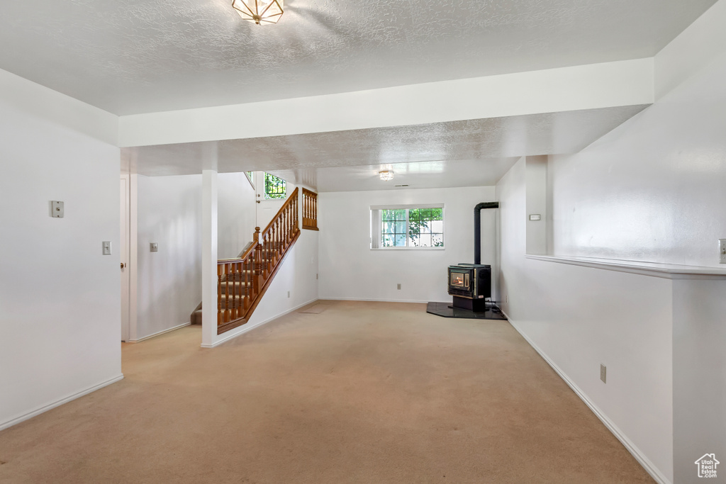 Basement featuring stairway, a wood stove, and light carpet
