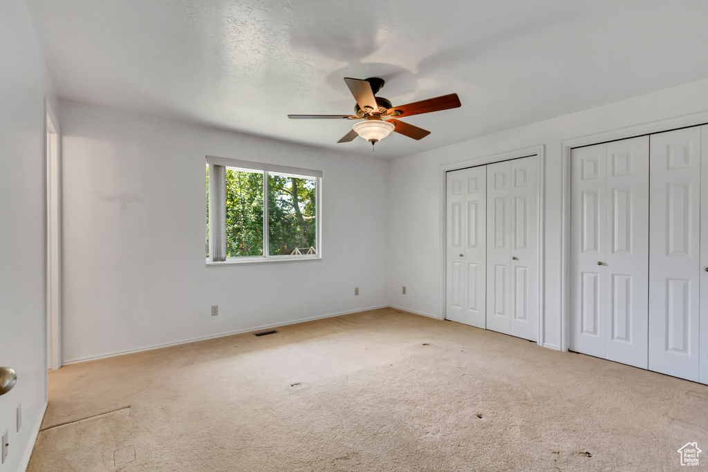 Unfurnished bedroom with multiple closets, carpet, and a ceiling fan
