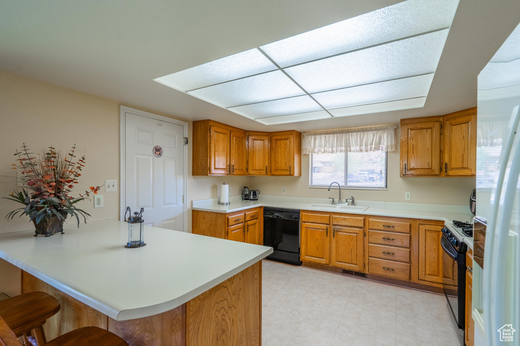 Kitchen with black appliances, a breakfast bar area, light countertops, and brown cabinetry