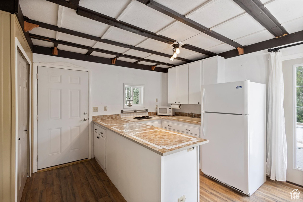 Kitchen featuring white appliances, wood finished floors, light countertops, white cabinetry, and a peninsula