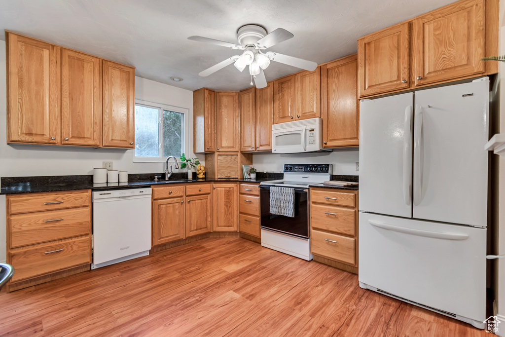 Kitchen with white appliances, light wood-style floors, dark countertops, and a ceiling fan