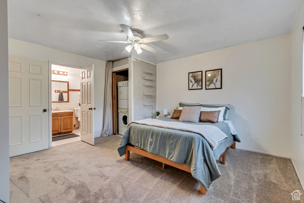 Bedroom featuring stacked washer and clothes dryer, light colored carpet, ensuite bathroom, and a ceiling fan