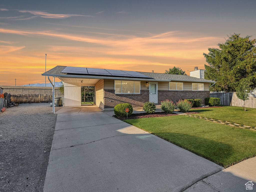 View of front of house featuring driveway, brick siding, an attached carport, a chimney, and solar panels
