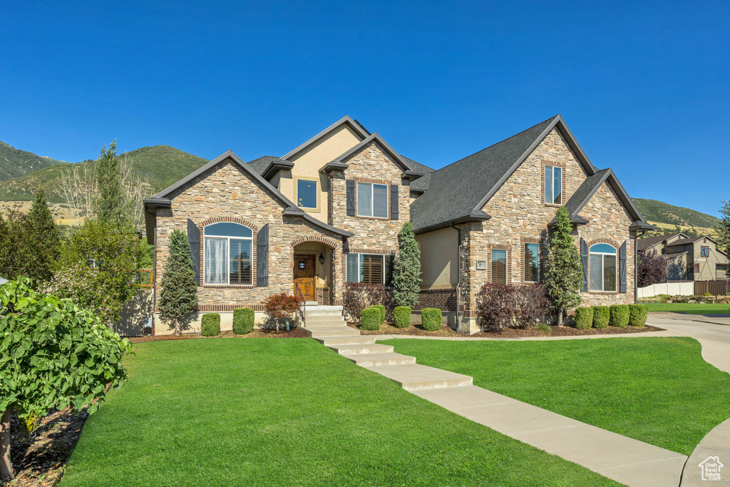 Craftsman-style home with stone siding, a front yard, a mountain view, and stucco siding