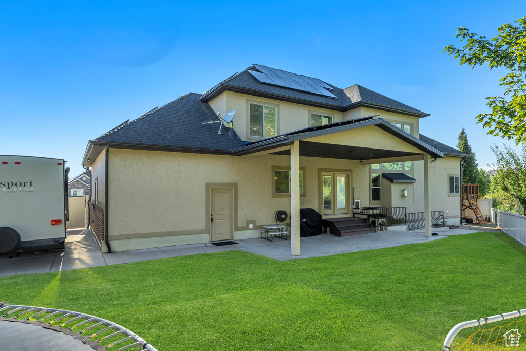 Rear view of property featuring stucco siding, solar panels, a patio, a fenced backyard, and a shingled roof