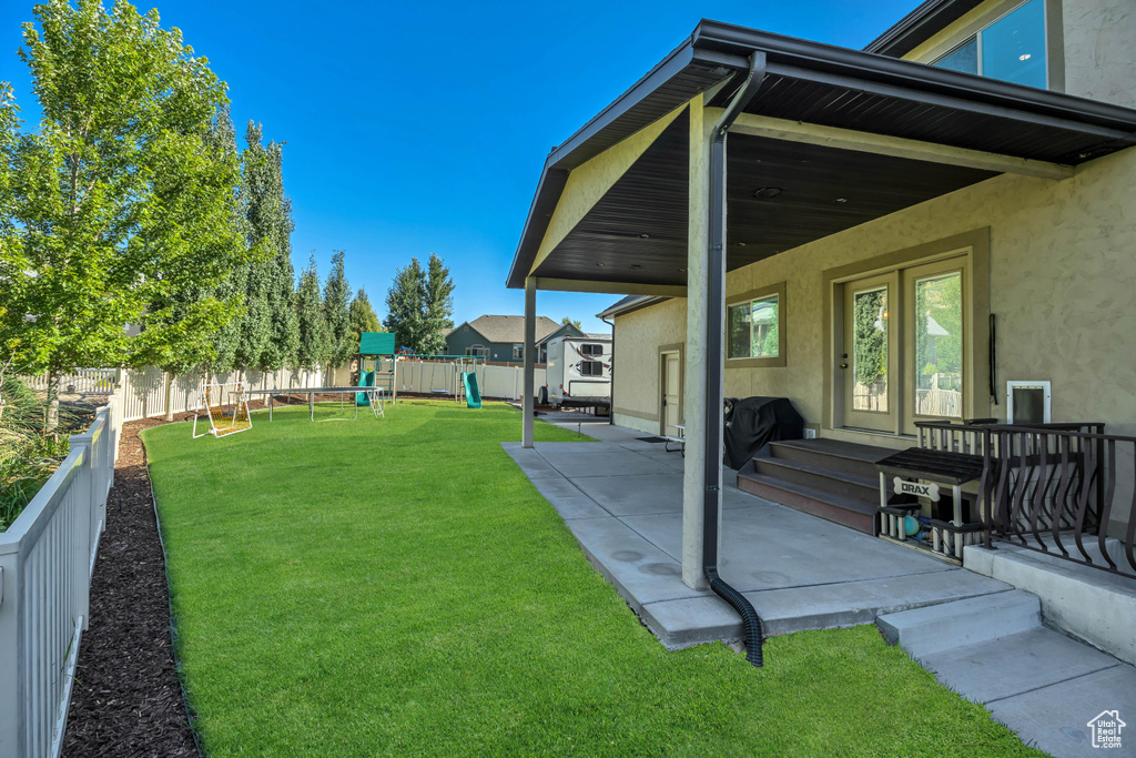 Fenced backyard featuring a playground and a patio area
