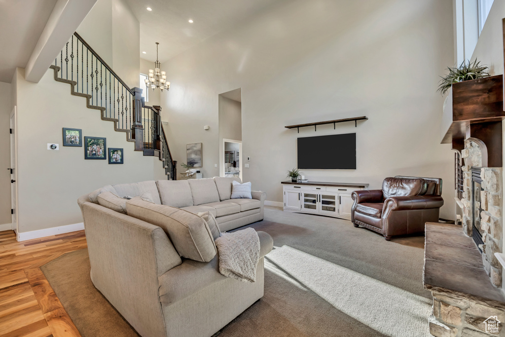 Living area featuring a high ceiling, stairway, a stone fireplace, a chandelier, and recessed lighting