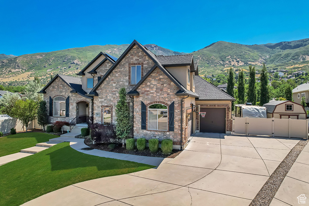 French country inspired facade featuring concrete driveway, a gate, a mountain view, an attached garage, and stone siding