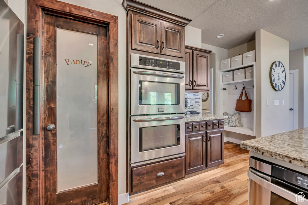 Kitchen featuring stainless steel double oven, light wood-style flooring, light stone countertops, a textured ceiling, and dark brown cabinets