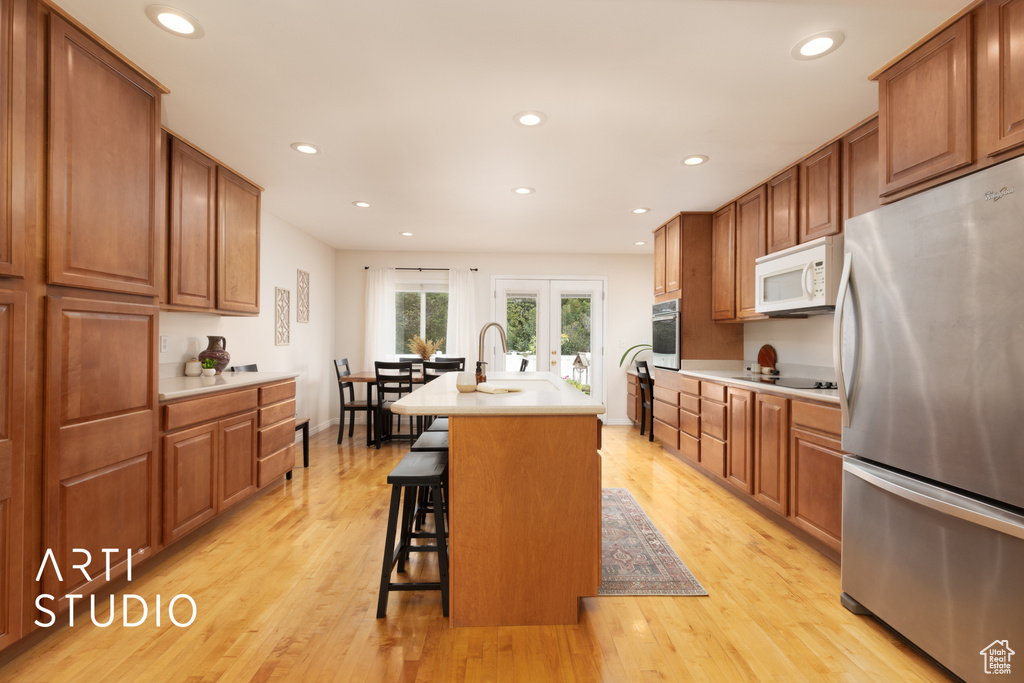 Kitchen featuring stainless steel appliances, light countertops, brown cabinetry, a breakfast bar area, and recessed lighting