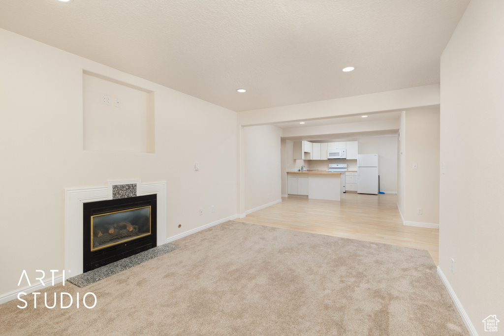 Unfurnished living room featuring light colored carpet, recessed lighting, a fireplace with flush hearth, and light wood-type flooring