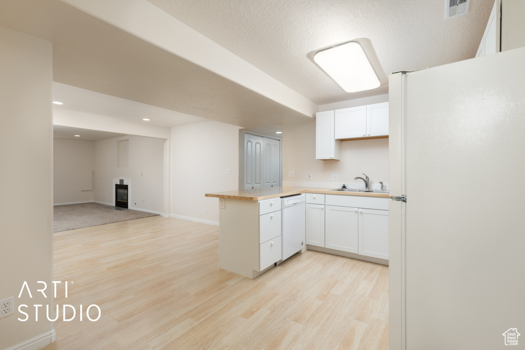 Kitchen featuring white appliances, light wood finished floors, a peninsula, white cabinets, and open floor plan