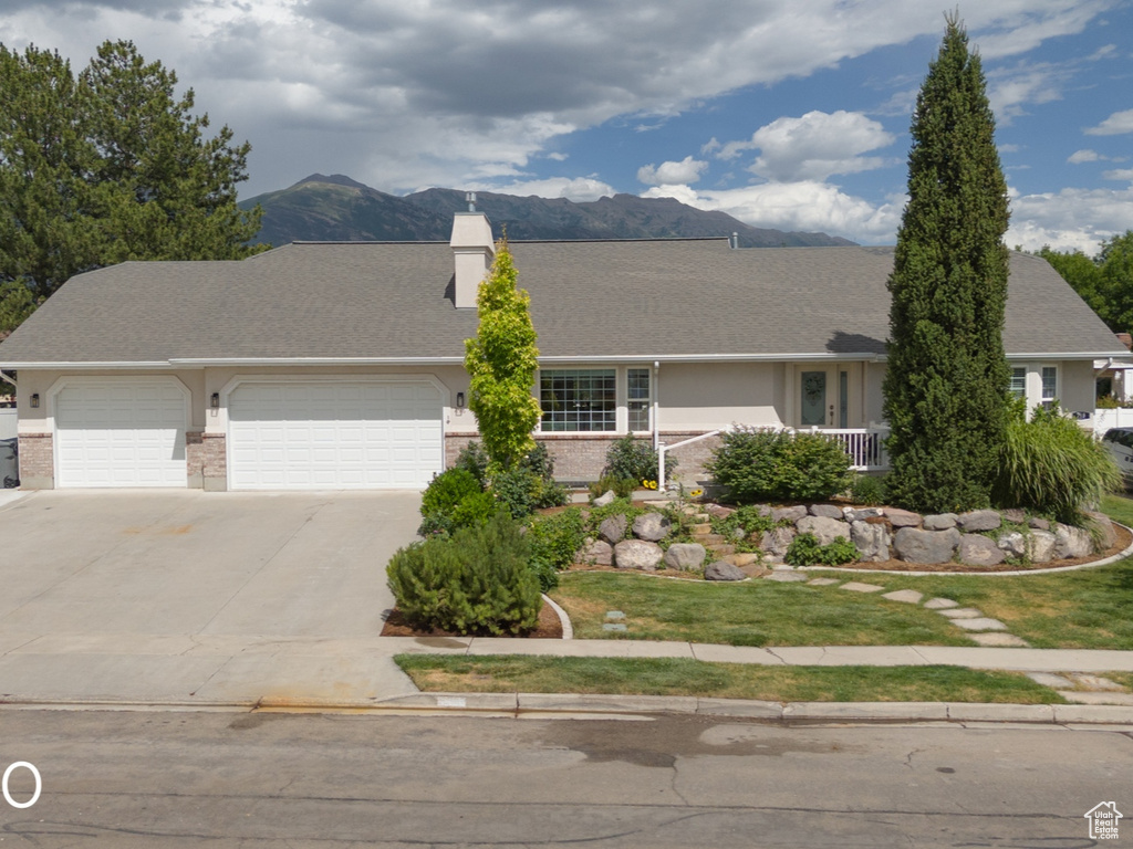 Ranch-style home with a garage, concrete driveway, a mountain view, a chimney, and brick siding