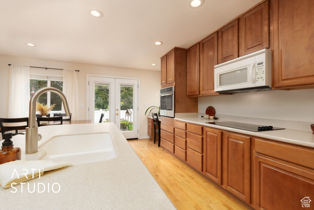 Kitchen featuring white microwave, black electric cooktop, oven, recessed lighting, and light countertops