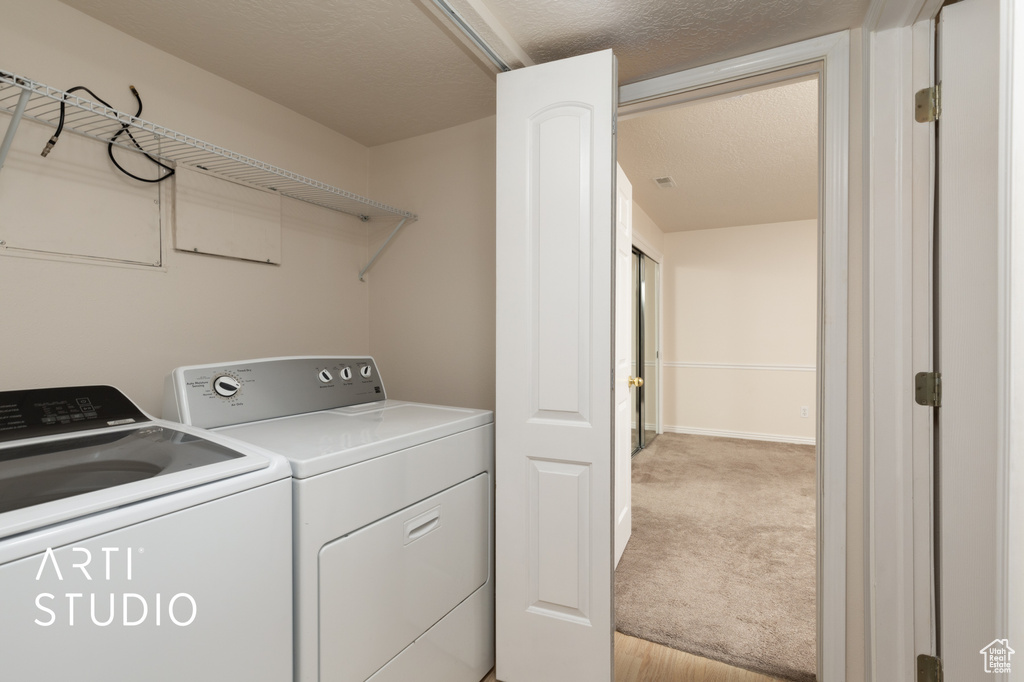Laundry area with washer and dryer, light colored carpet, and a textured ceiling