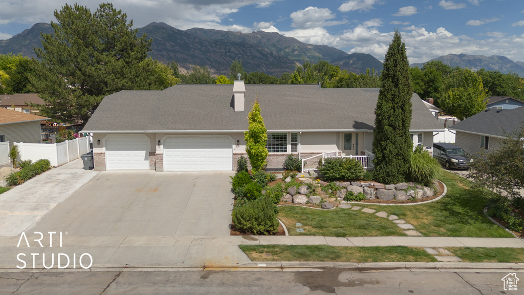 View of front of property with a garage, a mountain view, concrete driveway, a chimney, and brick siding