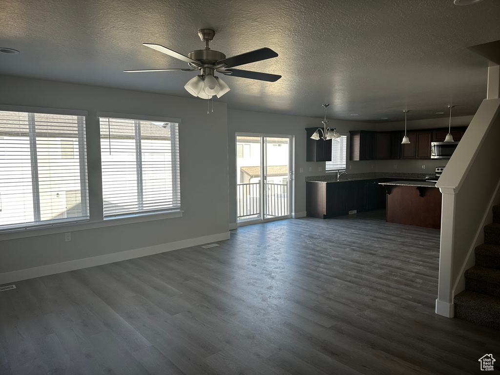 Unfurnished living room featuring dark wood-style floors, a textured ceiling, a chandelier, ceiling fan, and stairway