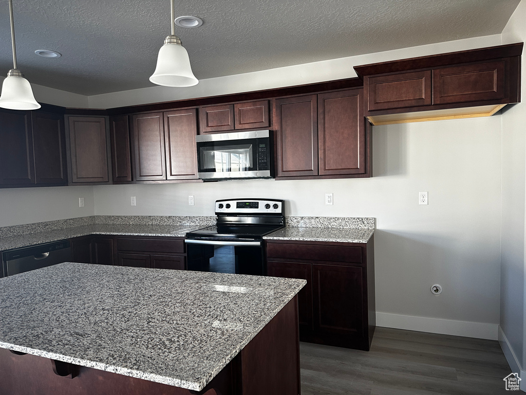 Kitchen featuring stainless steel microwave, range with electric stovetop, light stone countertops, wood finished floors, and a textured ceiling