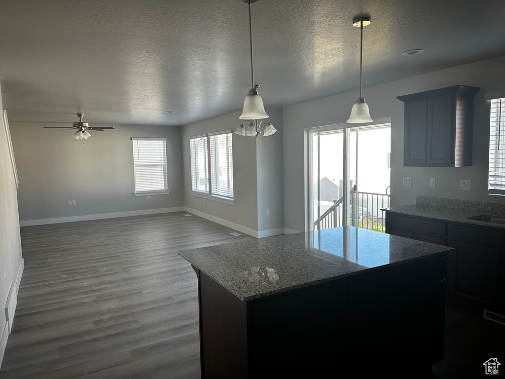 Kitchen with a textured ceiling, wood finished floors, a kitchen island, ceiling fan, and light stone countertops