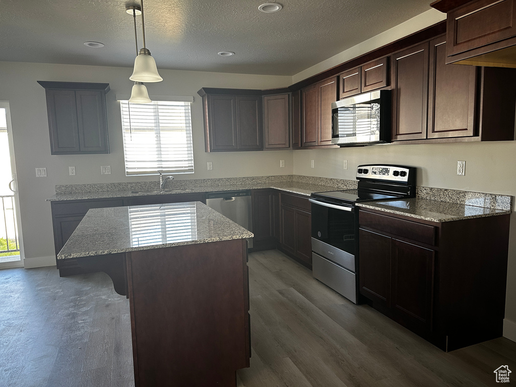 Kitchen featuring stainless steel appliances, a center island, wood finished floors, plenty of natural light, and a textured ceiling