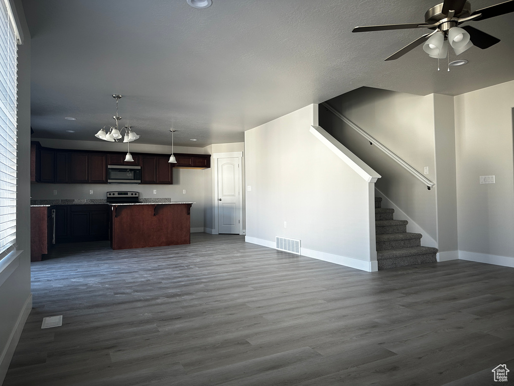 Kitchen with open floor plan, stainless steel appliances, a ceiling fan, dark wood-style flooring, and decorative light fixtures