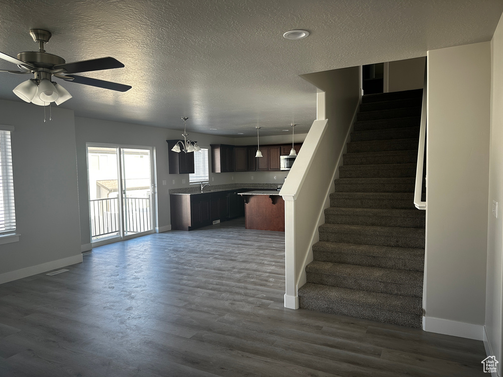 Unfurnished living room featuring stairway, a textured ceiling, dark wood-style flooring, a ceiling fan, and a chandelier