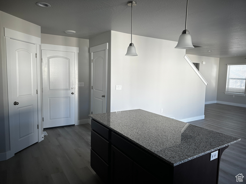 Kitchen featuring dark wood finished floors, a kitchen island, stone counters, open floor plan, and hanging light fixtures
