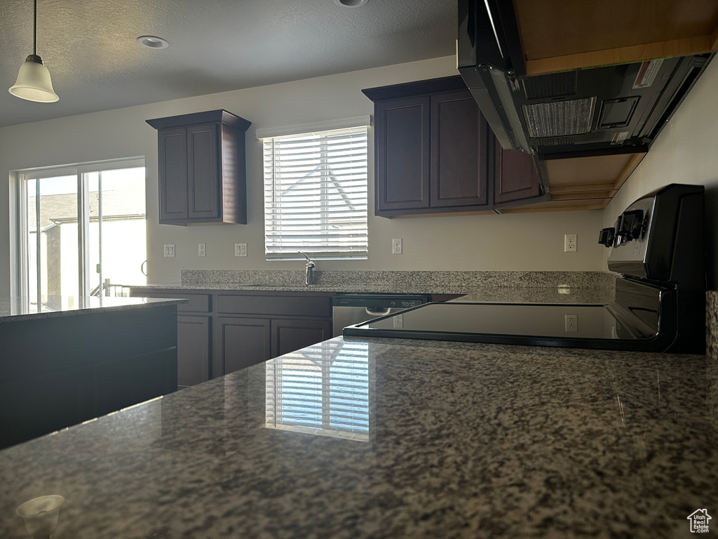 Kitchen featuring range hood, plenty of natural light, dark stone countertops, and hanging light fixtures