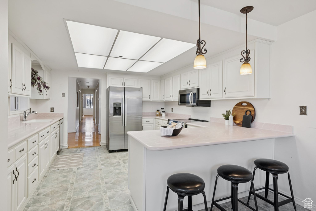 Kitchen featuring appliances with stainless steel finishes, a peninsula, white cabinetry, and light countertops