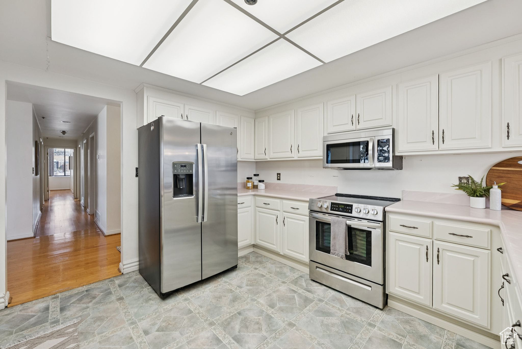 Kitchen with appliances with stainless steel finishes, light countertops, white cabinetry, and light wood-style floors