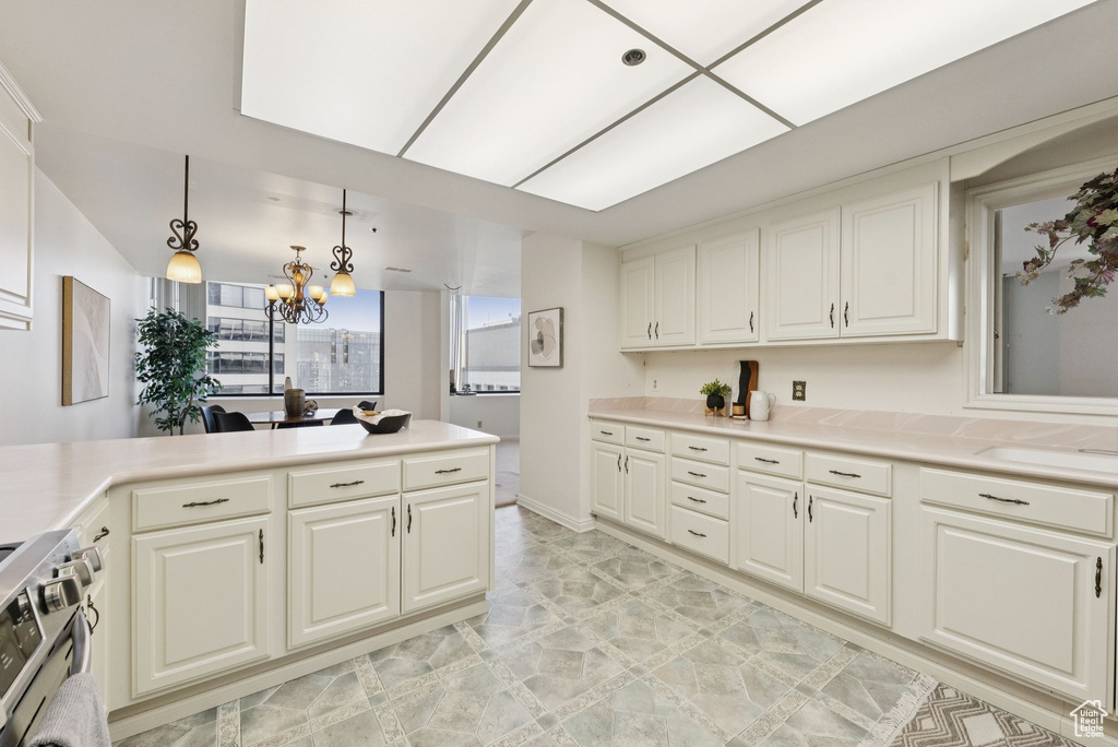Kitchen featuring stainless steel gas range, a chandelier, light countertops, a peninsula, and hanging light fixtures