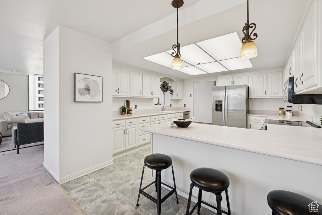 Kitchen featuring stainless steel appliances, a peninsula, light countertops, and white cabinetry