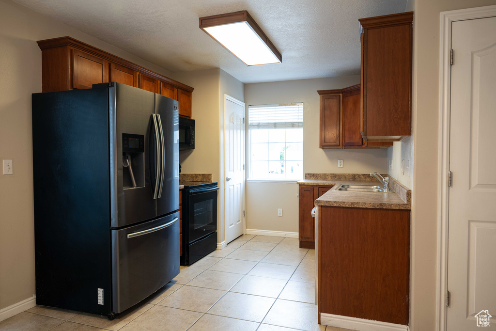 Kitchen with black appliances, brown cabinets, light tile patterned floors, and light countertops