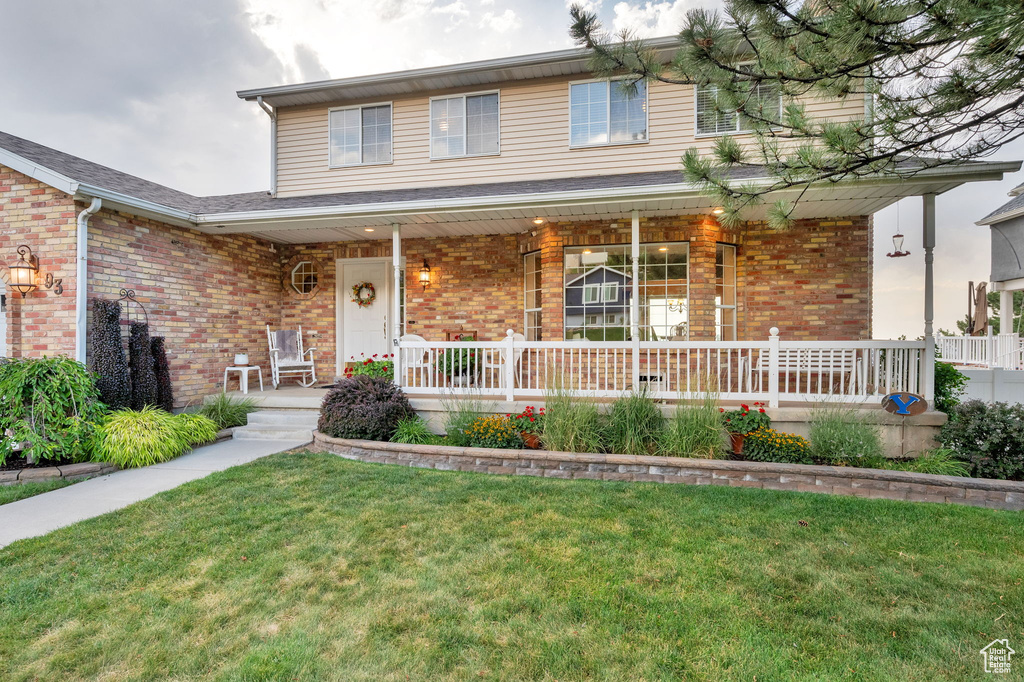 View of front facade featuring a porch, brick siding, and a front lawn