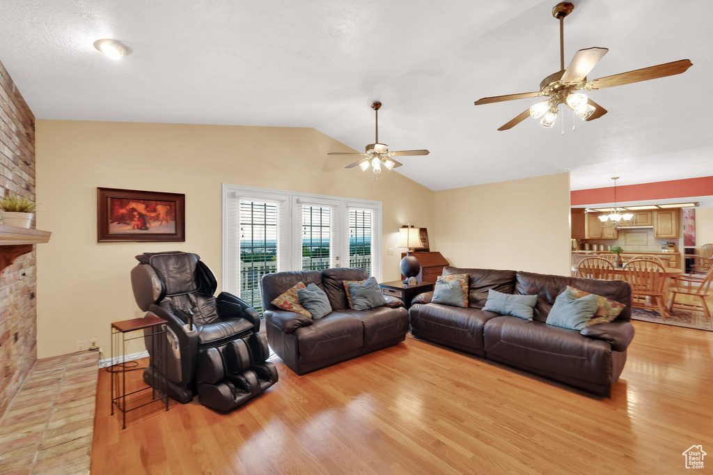Living area featuring vaulted ceiling, light wood-type flooring, a ceiling fan, and a chandelier