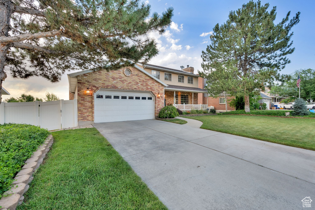 Traditional home featuring brick siding, covered porch, driveway, a garage, and a chimney