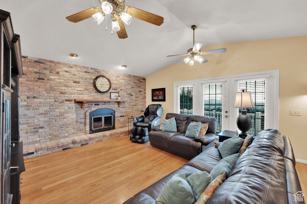 Living area with a ceiling fan, a brick fireplace, wood finished floors, and vaulted ceiling